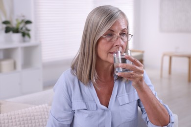 Senior woman in glasses drinking water at home