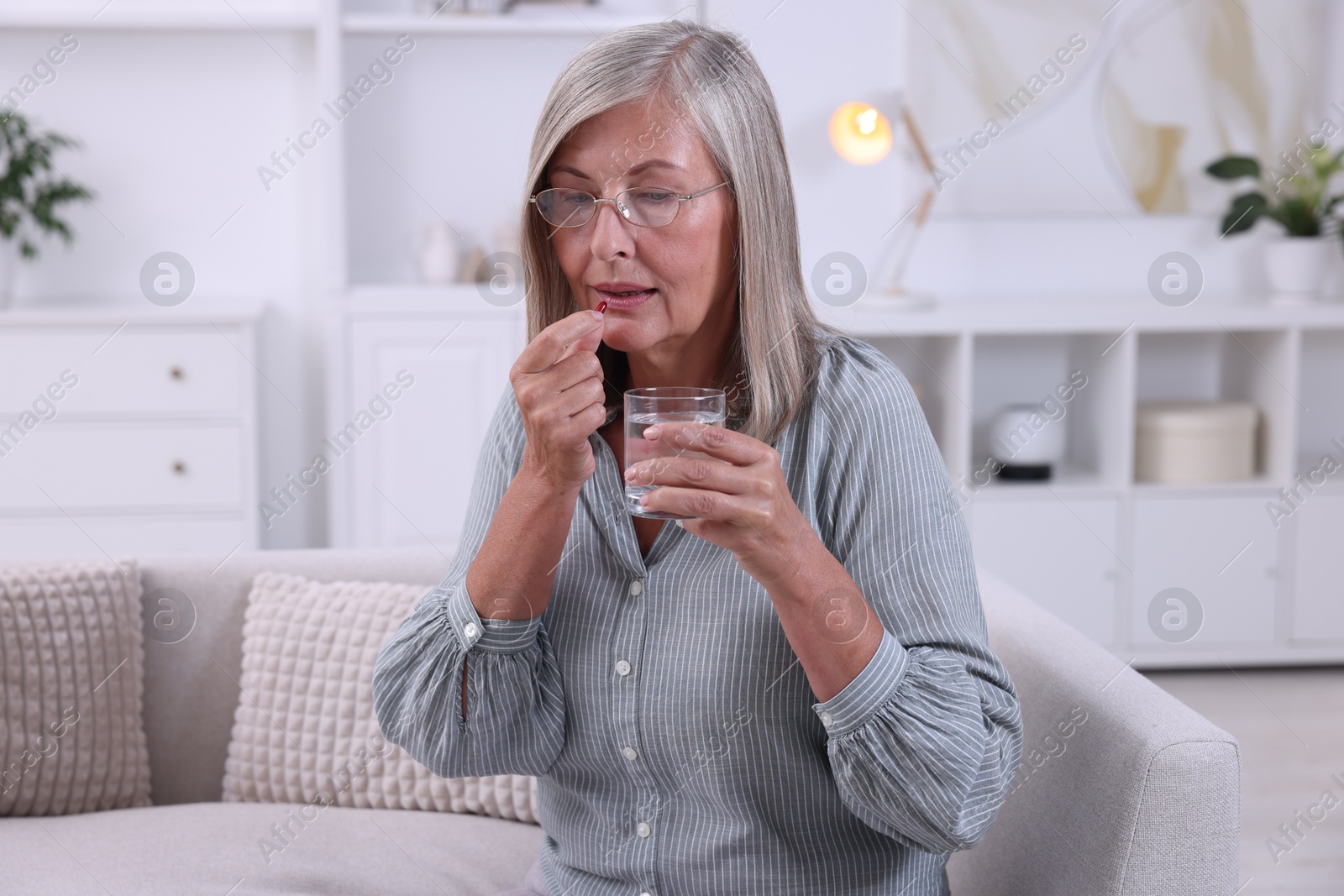 Photo of Senior woman with glass of water taking pill at home