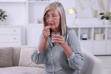 Senior woman with glass of water taking pill at home