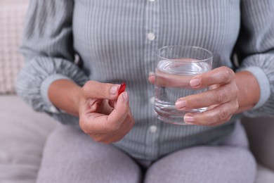 Senior woman with glass of water and pill at home, closeup