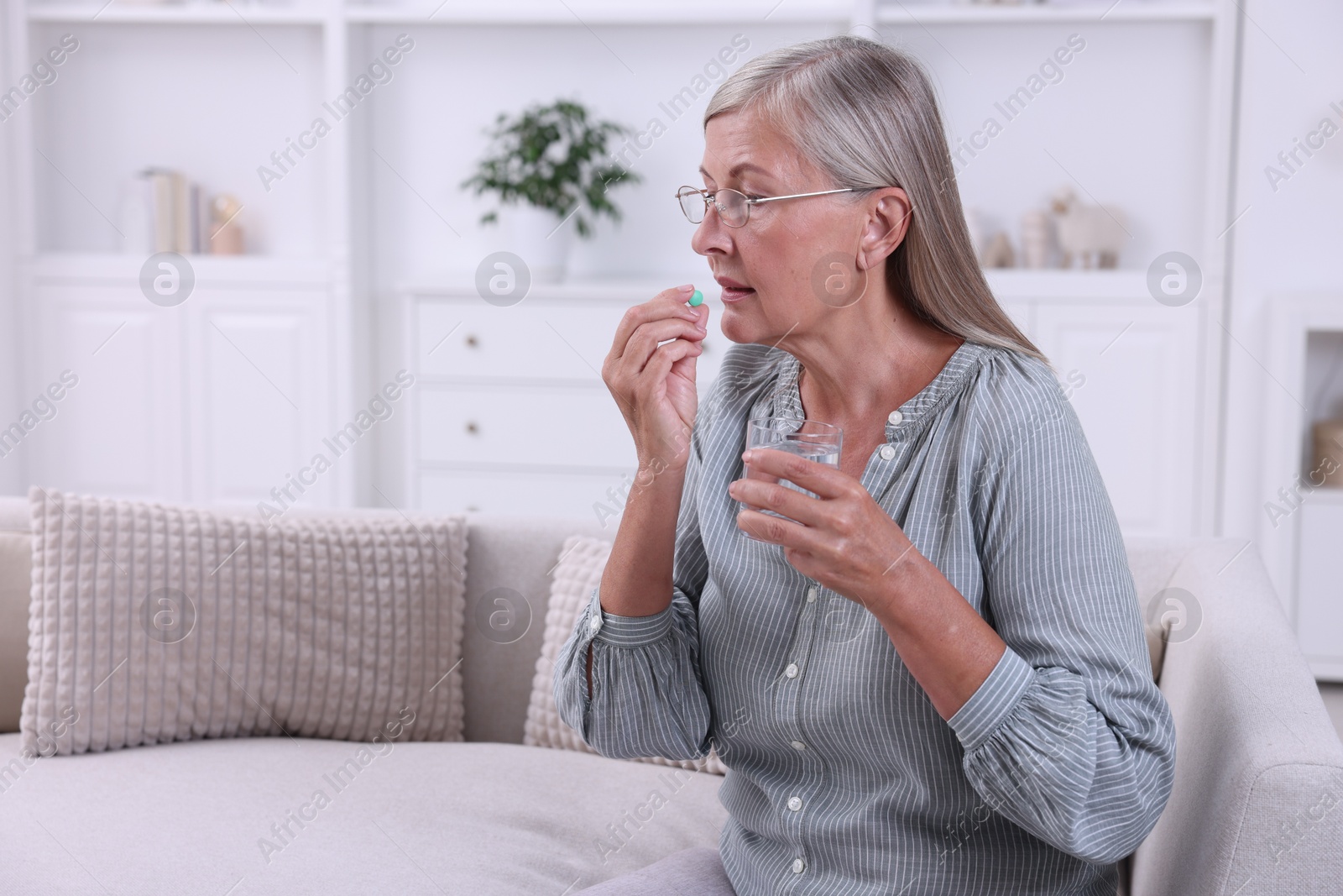 Photo of Senior woman with glass of water taking pill at home