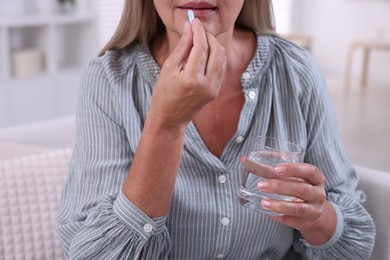 Photo of Senior woman with glass of water taking pill at home, closeup