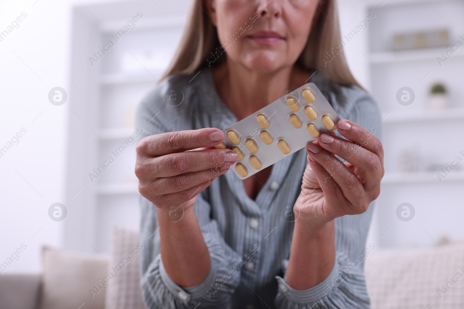 Photo of Senior woman holding blister with pills at home, closeup