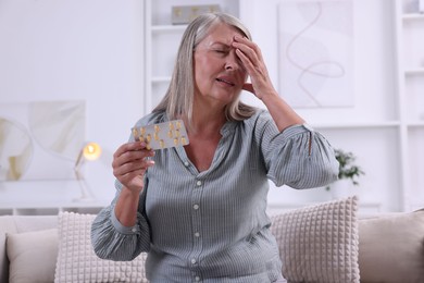 Senior woman holding blister with pills at home