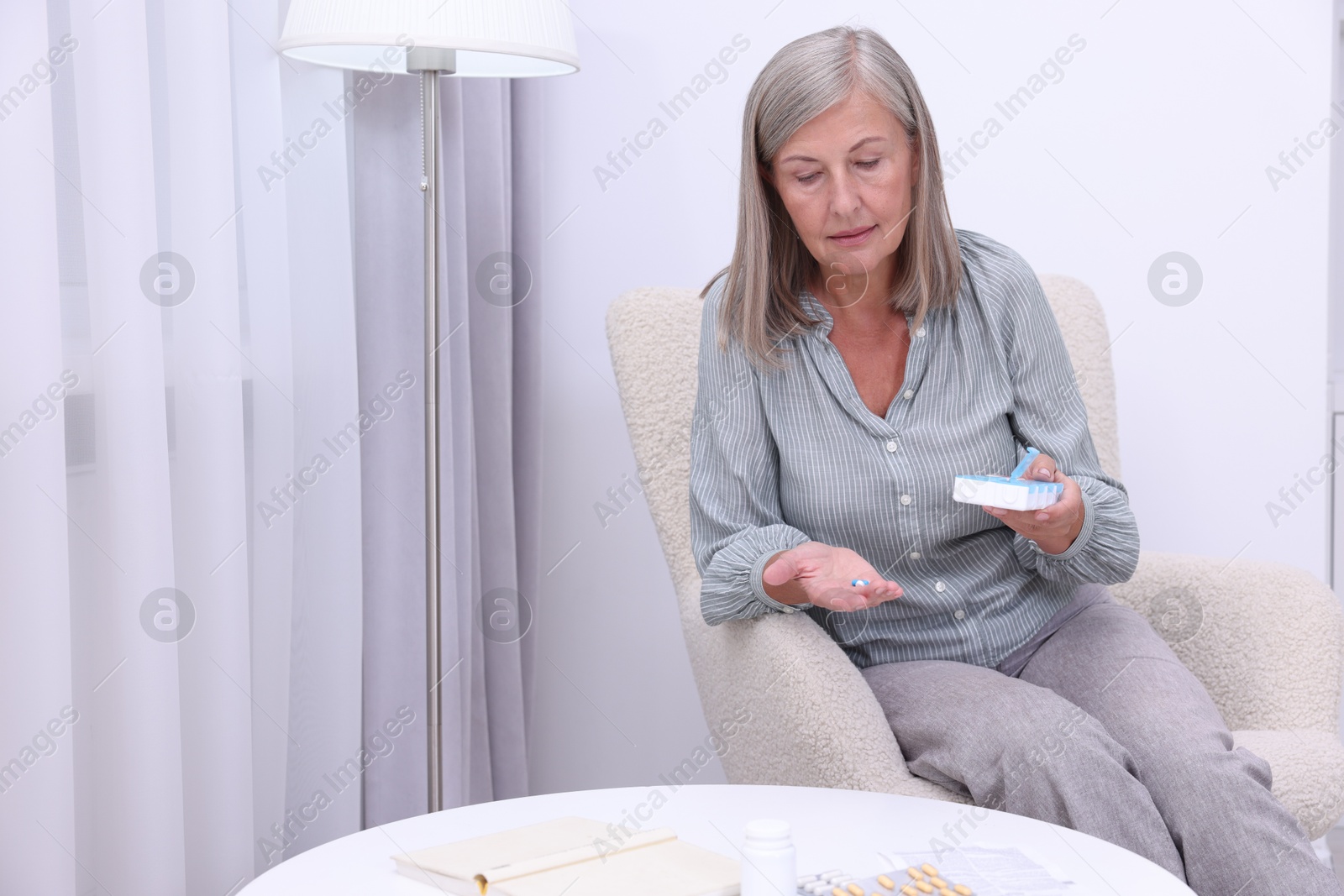 Photo of Senior woman with pills and organizer in armchair at home