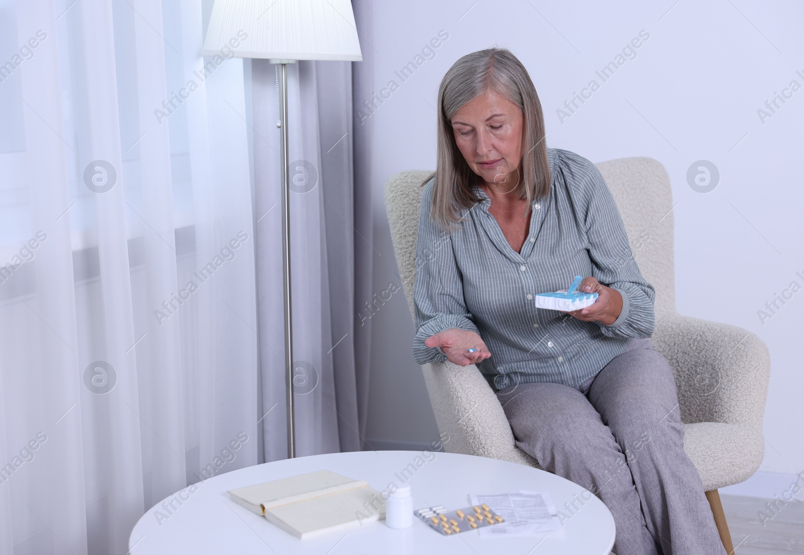 Photo of Senior woman with pills and organizer in armchair at home