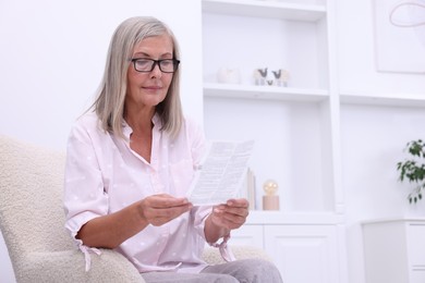 Senior woman reading medicine instruction in armchair at home