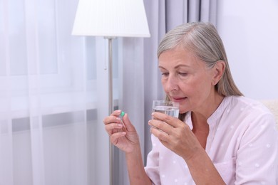 Photo of Senior woman with glass of water and pill at home, space for text