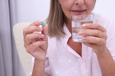 Photo of Senior woman with glass of water and pill at home, closeup