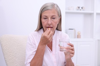 Photo of Senior woman with glass of water taking pill at home