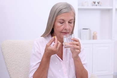 Senior woman with glass of water and pill at home