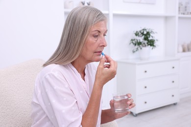 Senior woman with glass of water taking pill at home