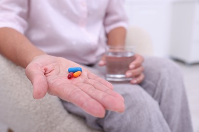 Photo of Senior woman with pills and glass of water at home, closeup