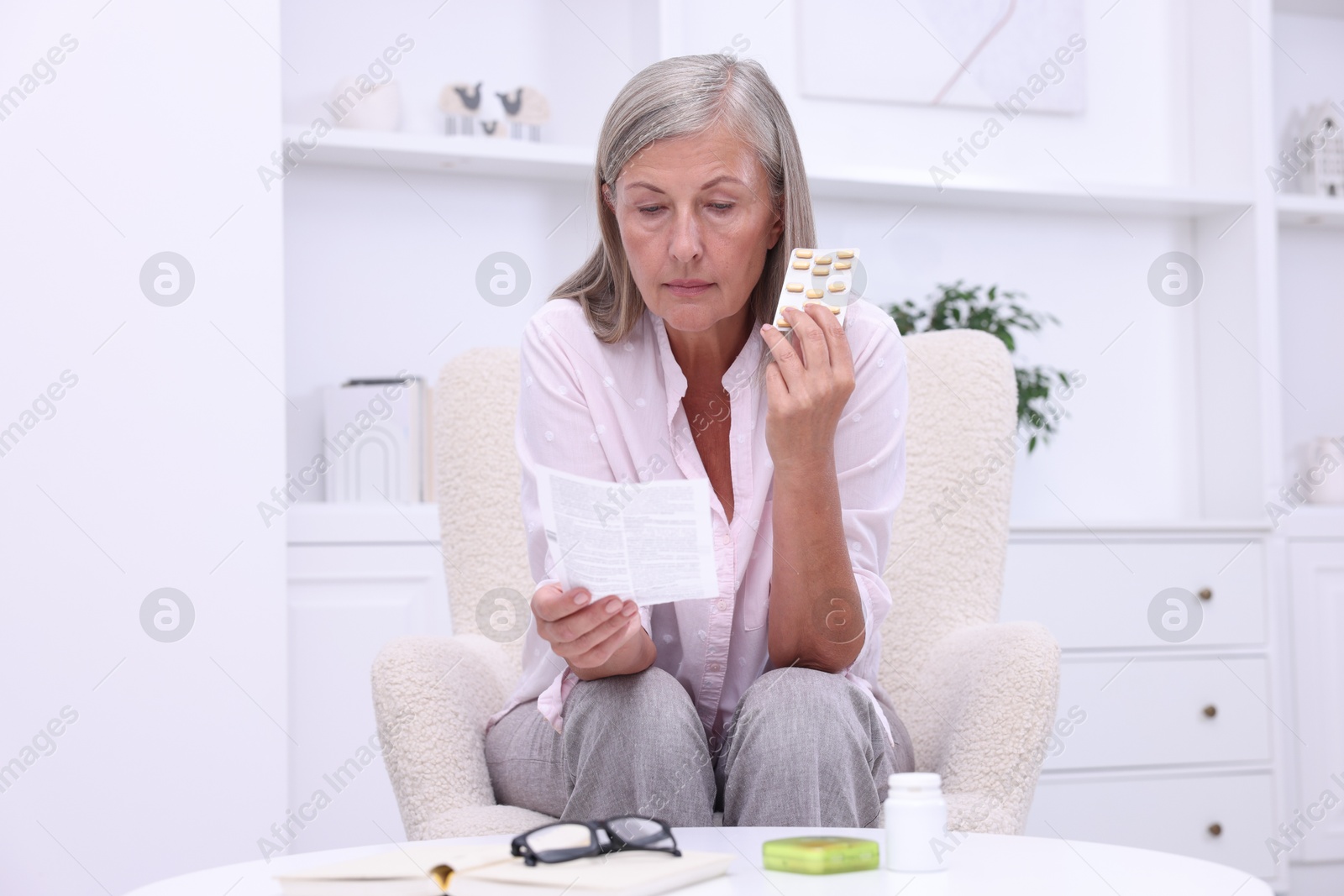 Photo of Senior woman with pills reading medicine instruction in armchair at home