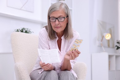 Senior woman with pills reading medicine instruction in armchair at home