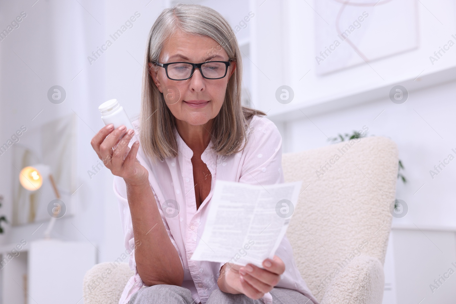 Photo of Senior woman with pills reading medicine instruction in armchair at home