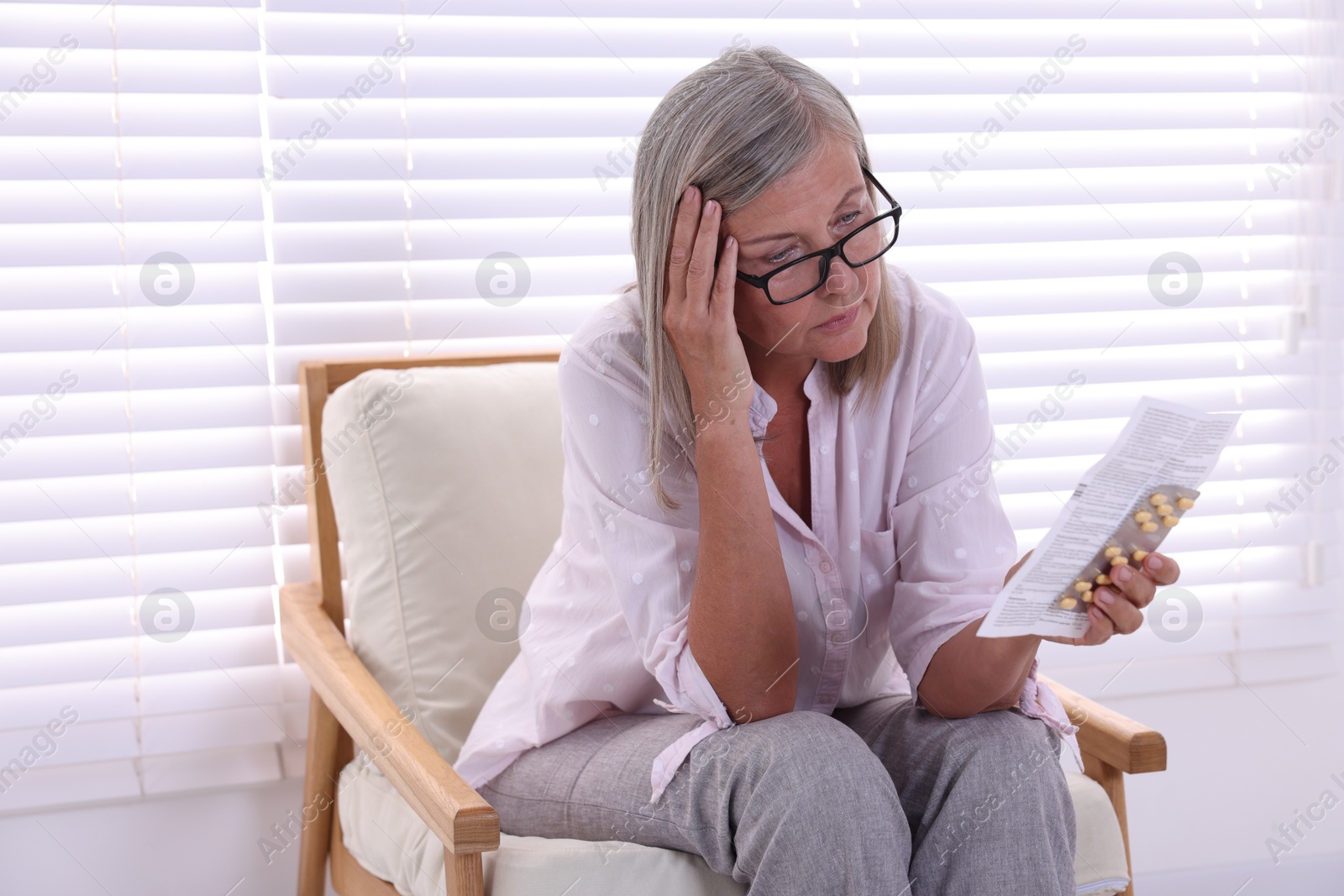 Photo of Senior woman with pills reading medicine instruction in armchair at home