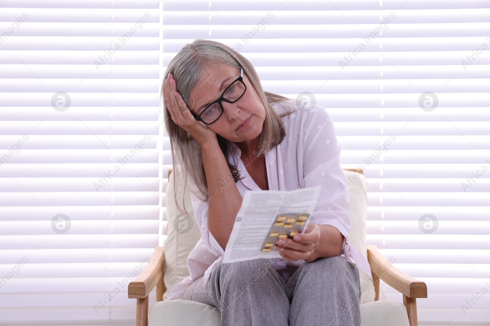 Photo of Senior woman with pills reading medicine instruction in armchair at home