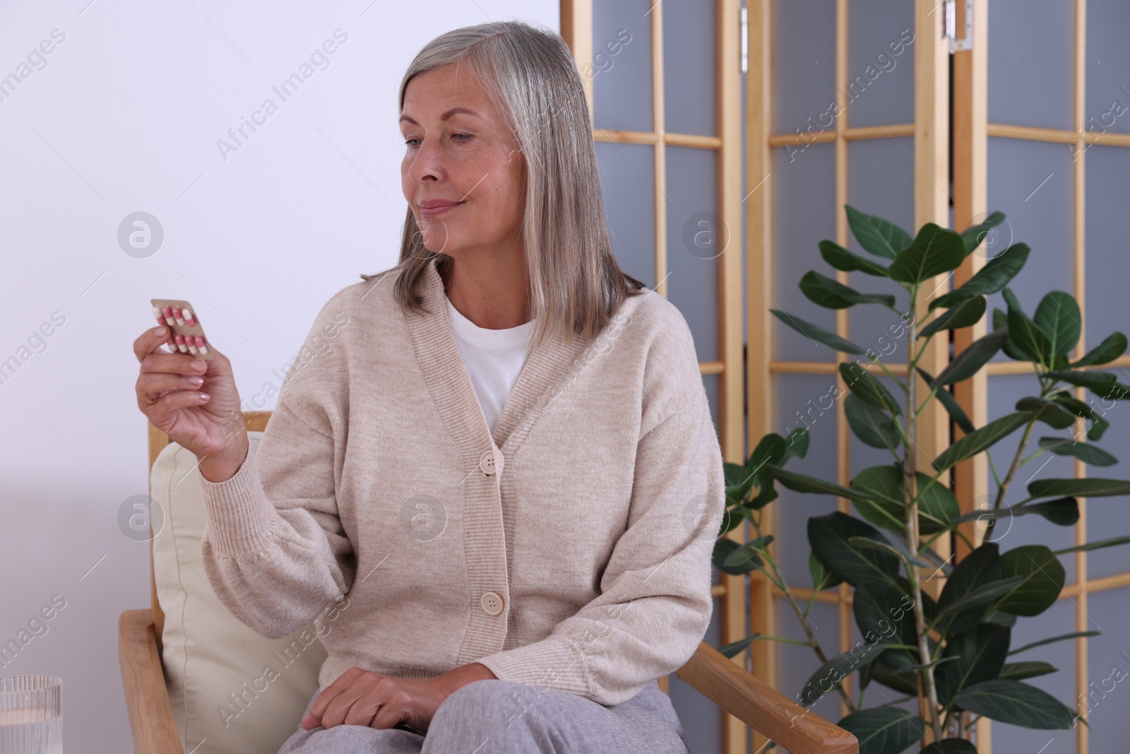 Photo of Senior woman holding blister with pills in armchair at home