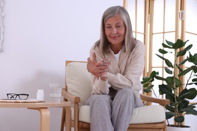 Senior woman holding blister with pills in armchair at home