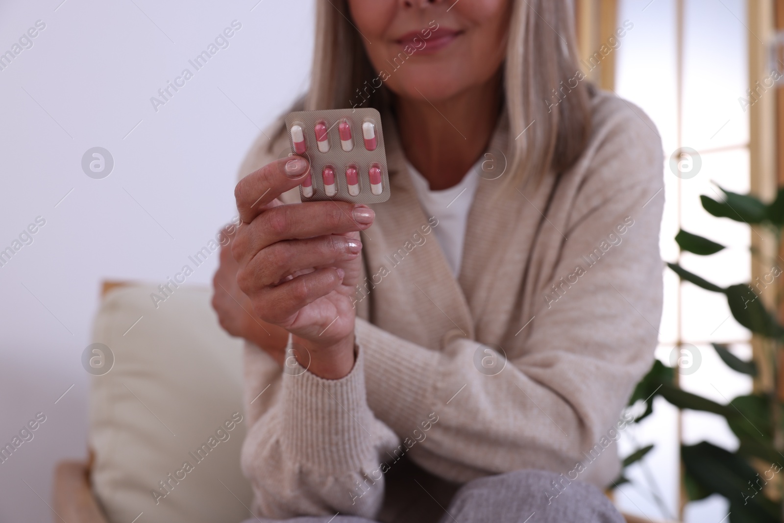 Photo of Senior woman holding blister with pills at home, closeup