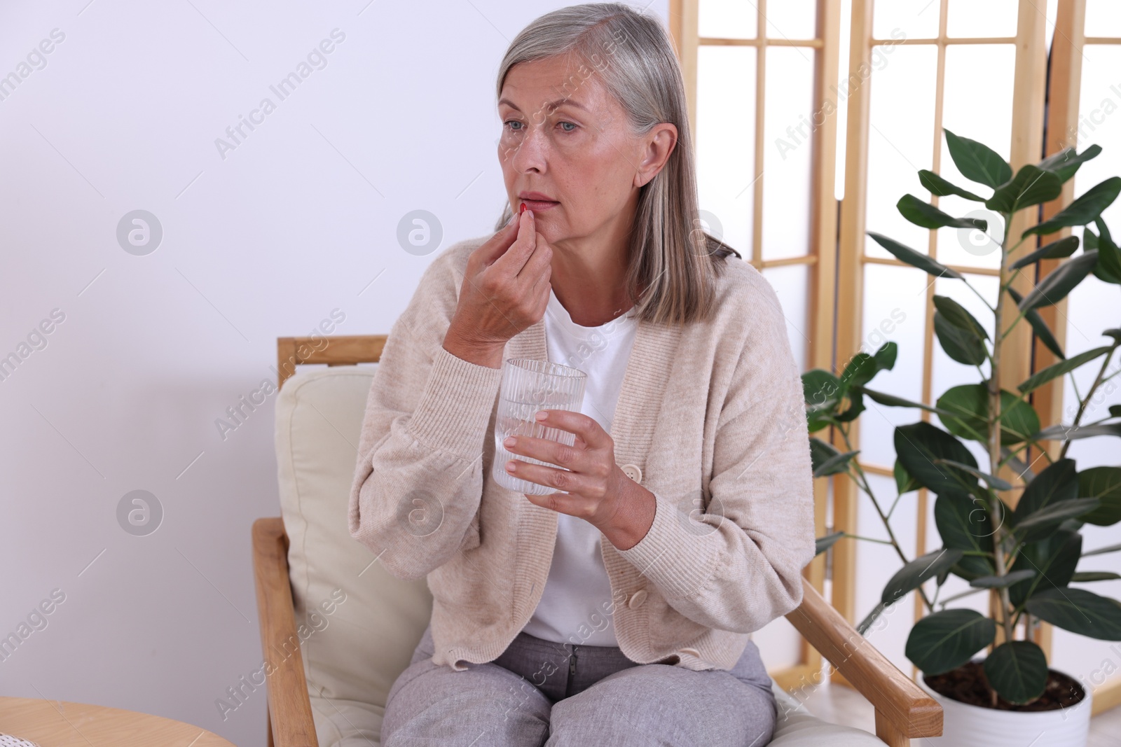 Photo of Senior woman with glass of water taking pill at home