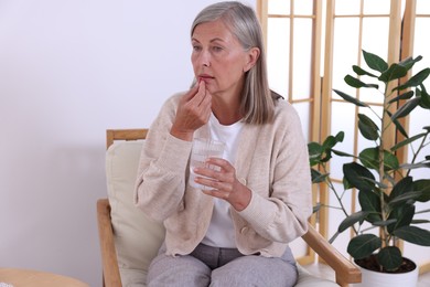 Senior woman with glass of water taking pill at home