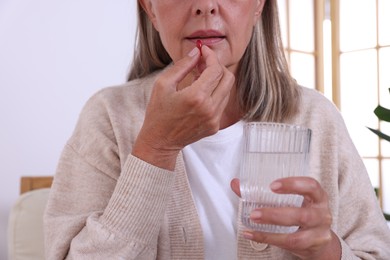 Photo of Senior woman with glass of water taking pill at home, closeup