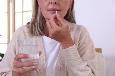 Photo of Senior woman with glass of water taking pill at home, closeup