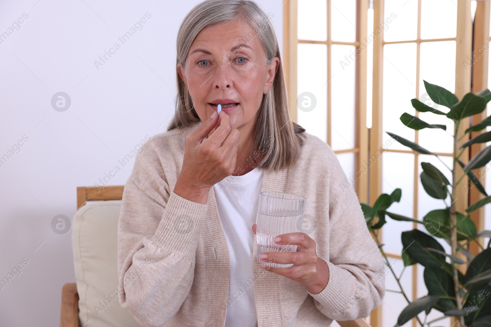 Photo of Senior woman with glass of water taking pill at home