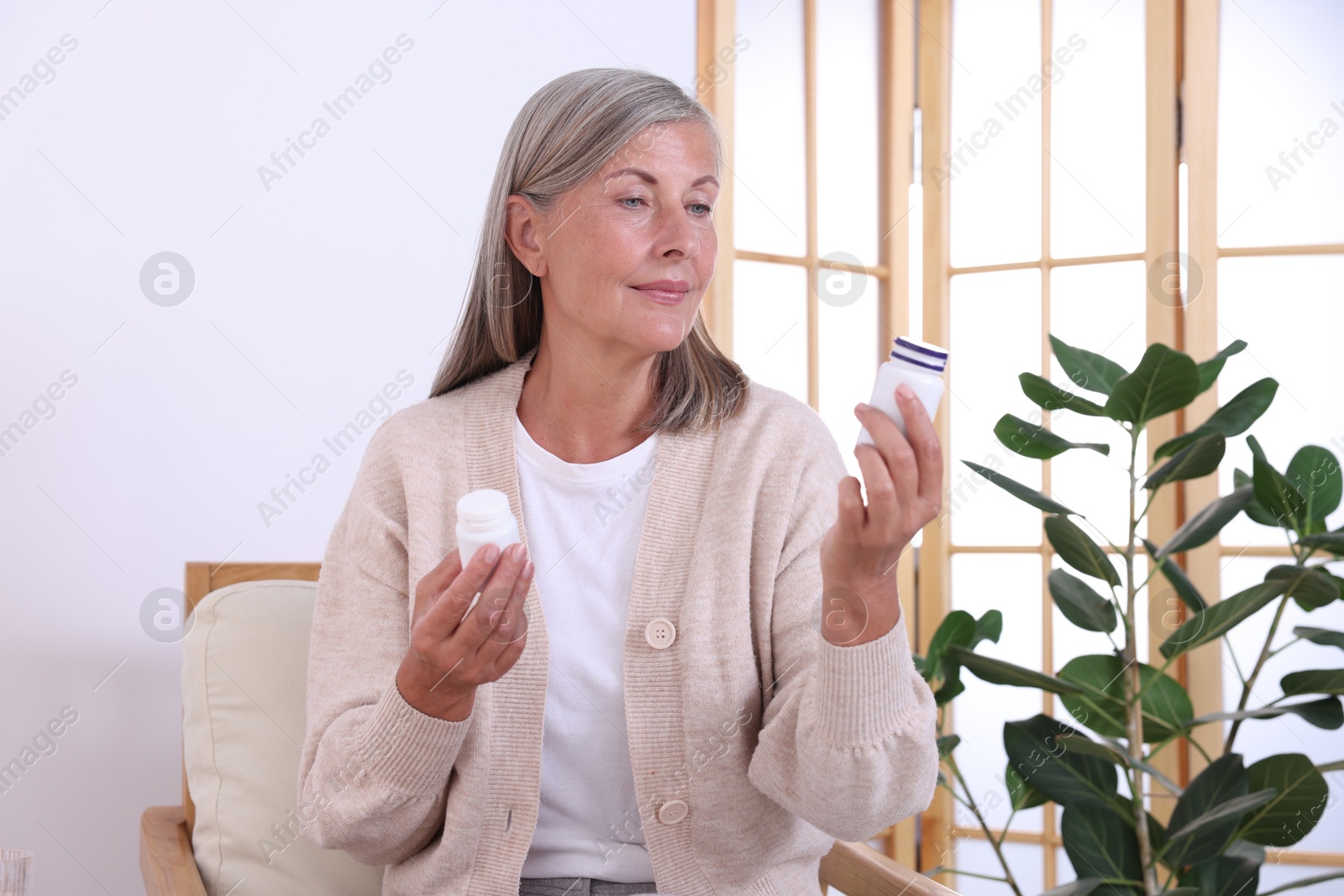 Photo of Senior woman with bottles of pills in armchair at home