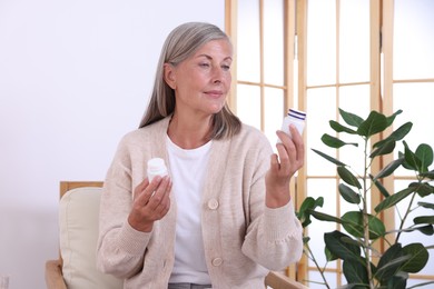 Senior woman with bottles of pills in armchair at home