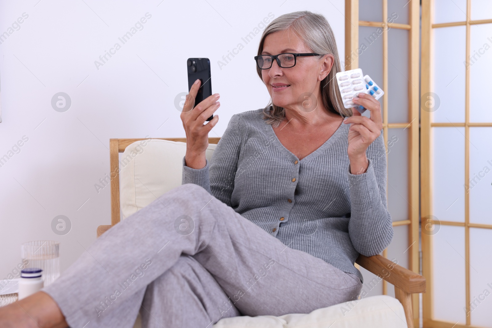 Photo of Senior woman with pills using smartphone at home