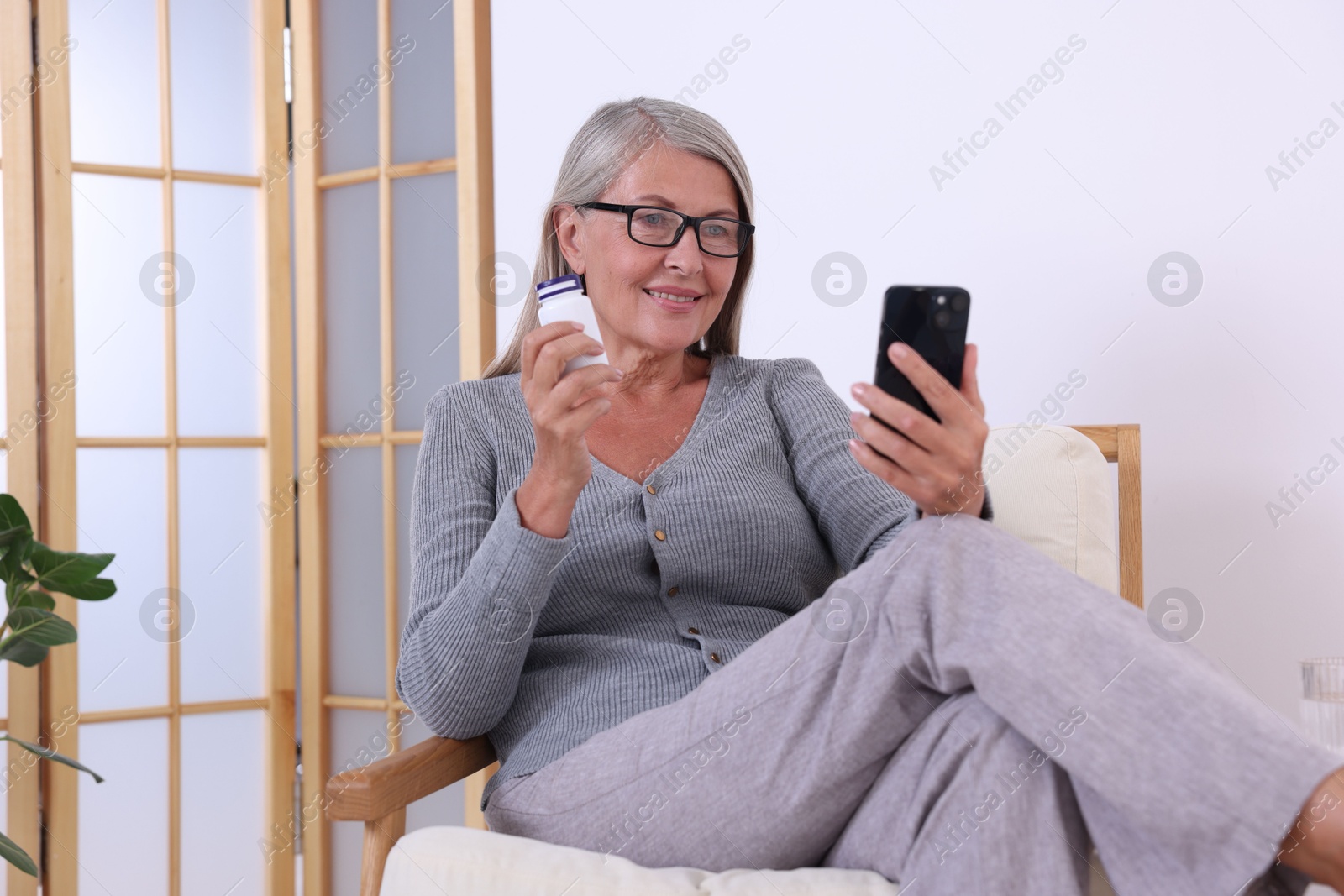 Photo of Senior woman with pills using smartphone at home