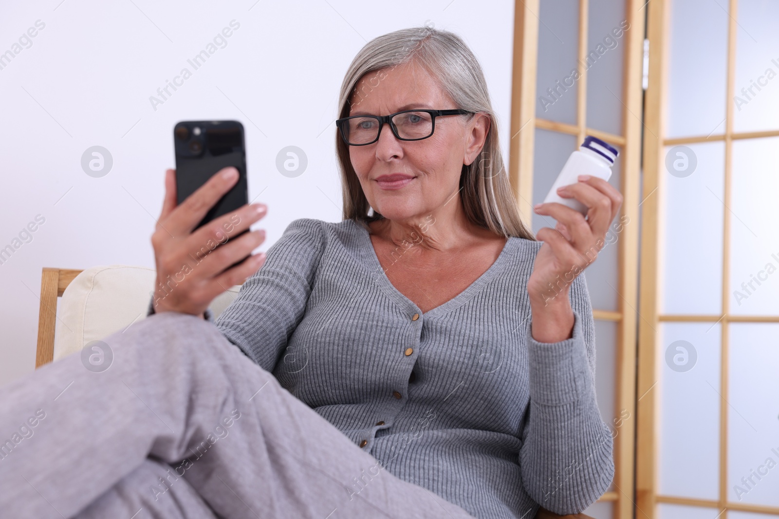 Photo of Senior woman with pills using smartphone at home