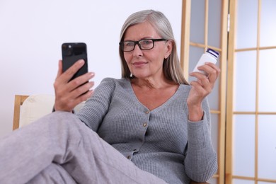 Photo of Senior woman with pills using smartphone at home