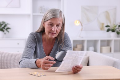 Senior woman with magnifying glass reading medicine instruction at table indoors