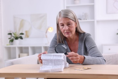 Photo of Senior woman with magnifying glass reading medicine instruction at table indoors