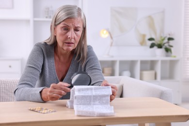 Photo of Senior woman with magnifying glass reading medicine instruction at table indoors