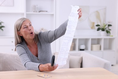 Senior woman with magnifying glass reading medicine instruction at table indoors