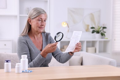 Senior woman with magnifying glass reading medicine instruction at table indoors