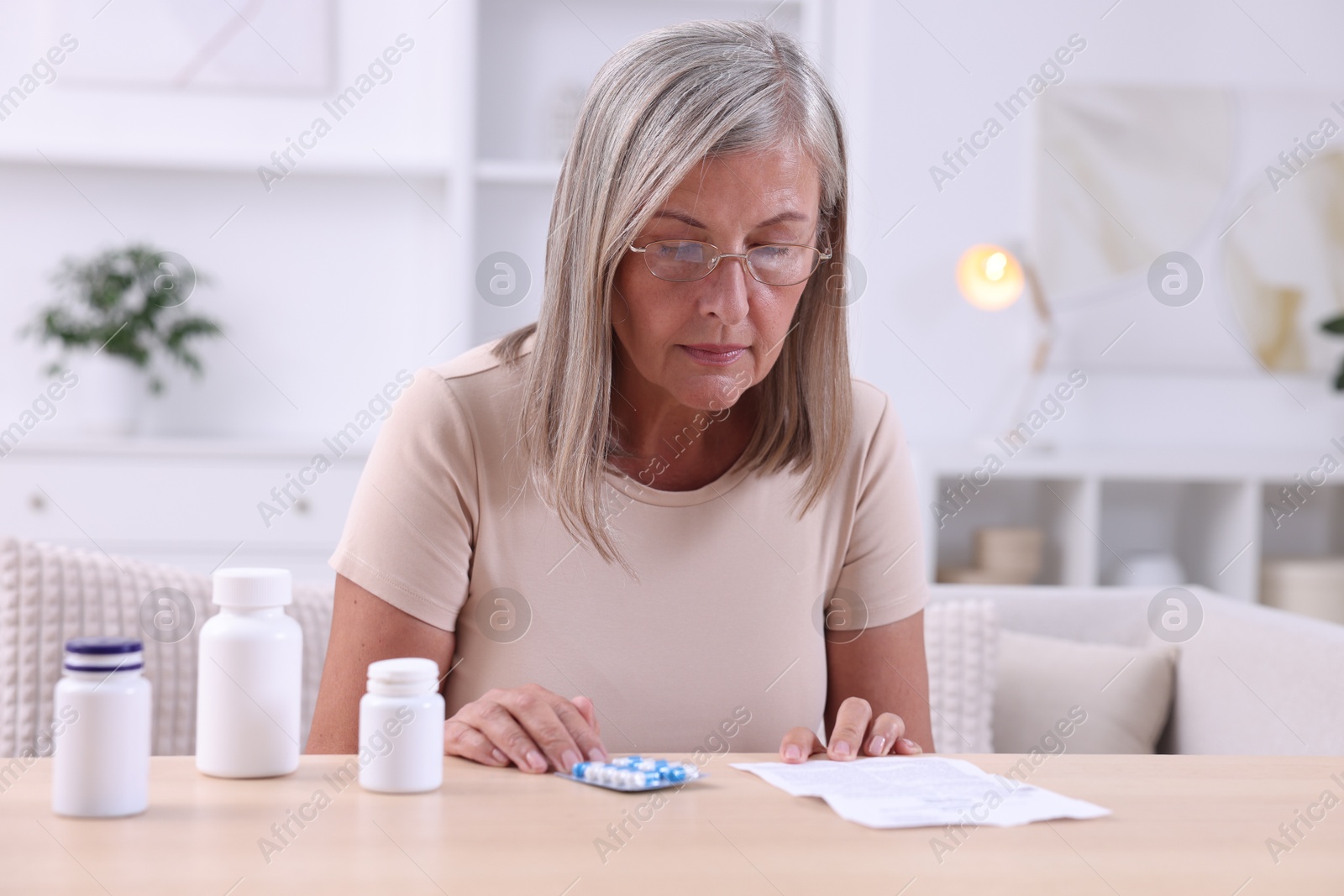 Photo of Senior woman reading medicine instruction at table indoors