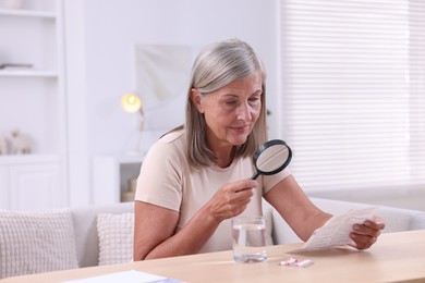 Senior woman with magnifying glass reading medicine instruction at table indoors