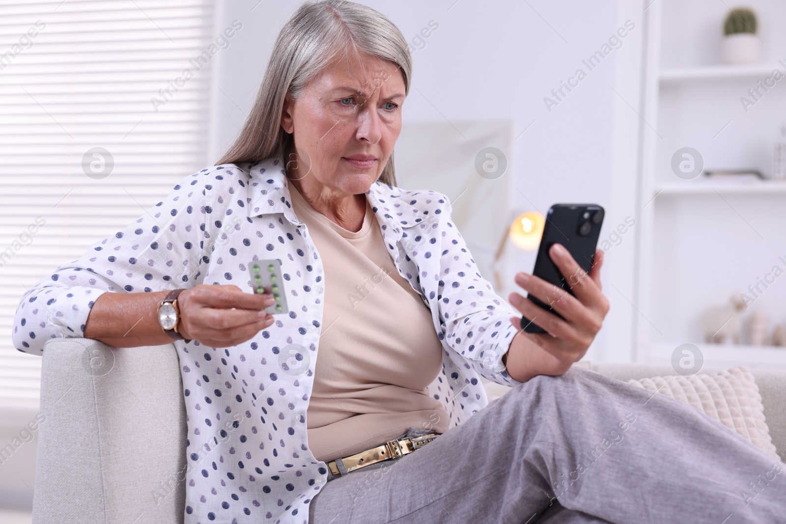 Photo of Senior woman with pills using smartphone on sofa at home