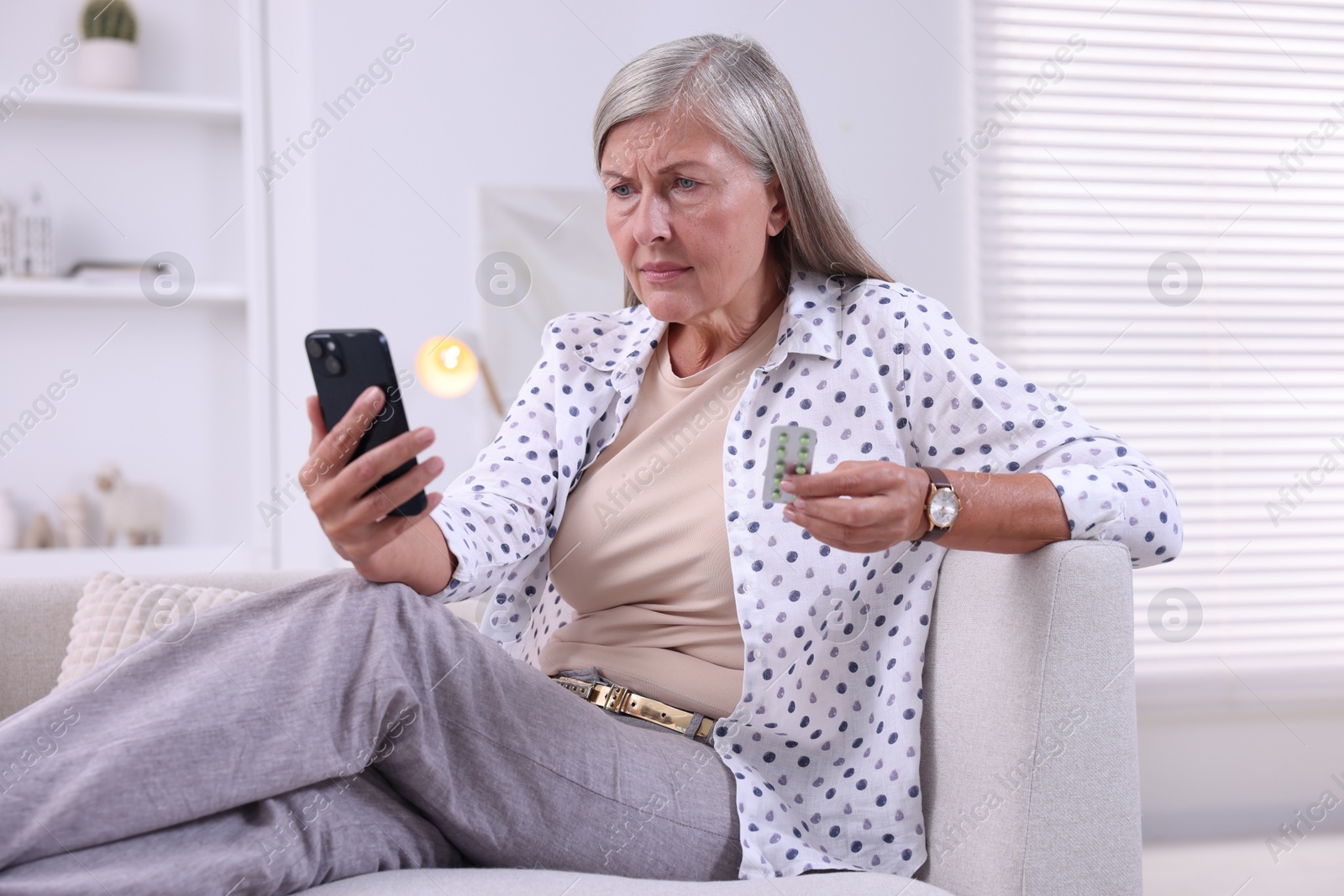 Photo of Senior woman with pills using smartphone on sofa at home