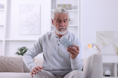 Photo of Senior man holding blister with pills at home