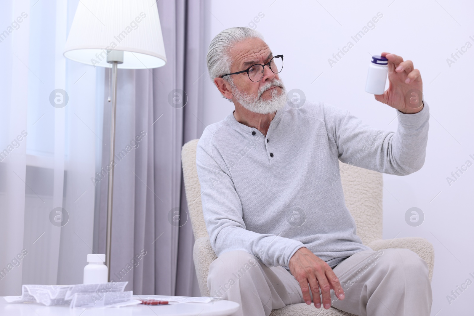 Photo of Senior man with bottle of pills in armchair at home