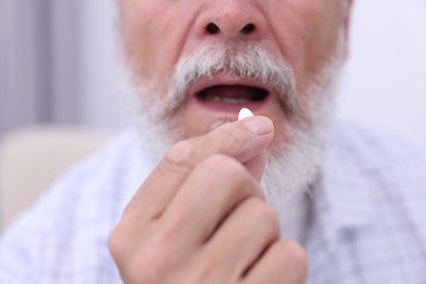 Senior man taking pill at home, closeup