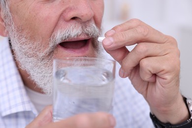 Photo of Senior man with glass of water taking pill at home, closeup