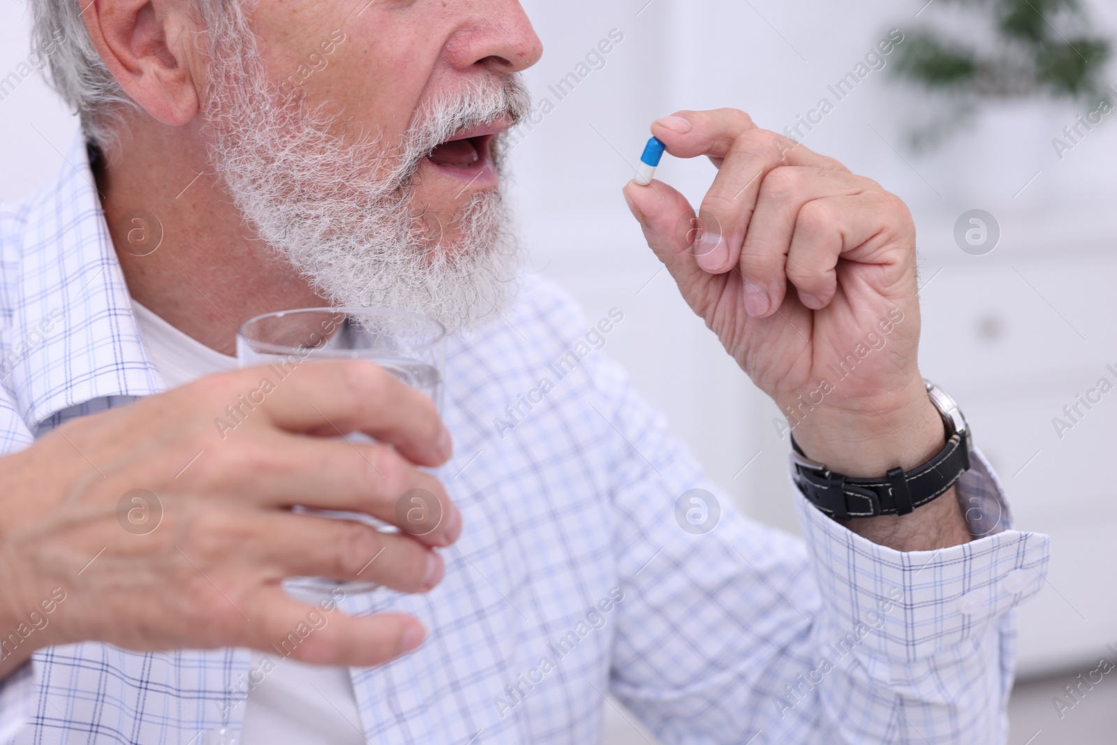 Photo of Senior man with glass of water taking pill at home, closeup